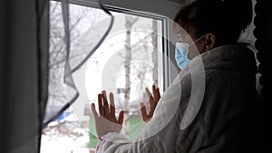 Old illness woman grandmother mother in medical mask stay at home looks sadness thoughtful out of window at street, hand