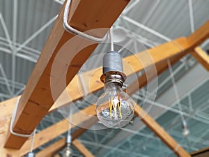 An old Incandescent light bulb close up. Light bulb hanging on wooden beam hanging on a rope. Vintage Industrial Lighting