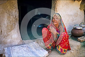 Old Indian woman crouching on the ground in front of her poor house. Rajasthan, Uttar Pradesh, India