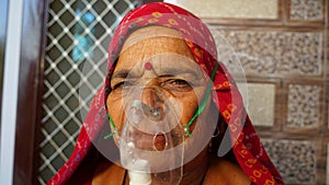 Old Indian woman infected with Covid 19 disease. Patient inhaling oxygen wearing mask with liquid Oxygen flow