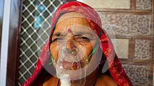 Old Indian woman infected with Covid 19 disease. Patient inhaling oxygen wearing mask with liquid Oxygen flow photo
