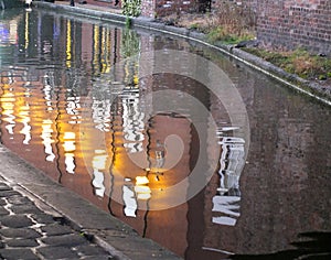 Old industrial buildings reflected in the canal in chester at twilight with illuminated windows