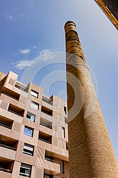 old industrial chimney on blue sky with clouds and modern building on its right