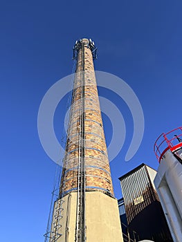 An old industrial chimney built of brick, reinforced with hoops, with built-in antennas against the blue sky