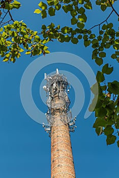 Old industrial chimney made of brick without smoke, with antennas, against the blue sky