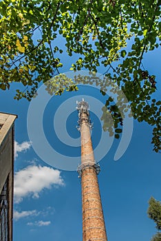 Old industrial chimney made of brick without smoke, with antennas, against the blue sky