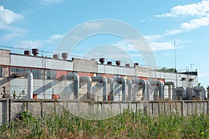 Old industry plant with pipes and tubes. Outside view of manufacturing complex under blue cloud sky. Concrete walls, metal frames