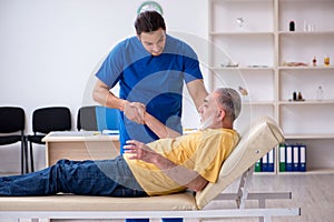 Old injured man visiting young male doctor chiropractor