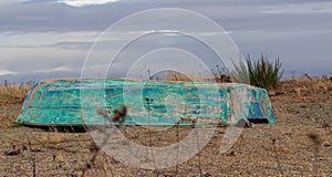 The old inverted green color boat lies on the sea shore in cloudy day