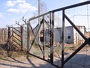 An old iron fence with a closed rusty gate prohibits travel to the territory of an abandoned technical station photo