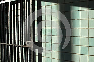 Old iron gate in subway station with shadows on green dirty tile wall