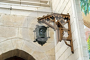 Old iron lantern with a cross hanging from a wooden frame on a stone wall of an old church