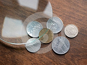 Old Italian Lira coins under magnifying glass on a wooden table. Local currencies that ceased to exist