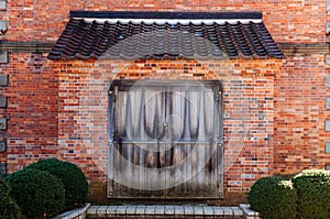 Old Japanese wooden gate with red brick wall and green shrubs