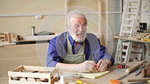 Old journeyman with many wrinkles sitting at the desk with tools.
