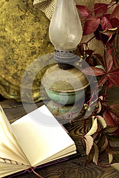 Old kerosene lamp and tray ,open notebook and red leaves of grapes on a wooden table in rustic style photo