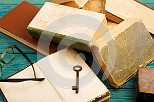 Old key, glasses and stack of antique books on blue wooden background