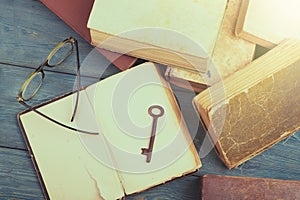 Old key, glasses and stack of antique books on blue wooden desk