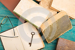 Old key, glasses and stack of antique books on blue wooden desk