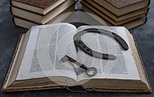 An old key and an old horseshoe rest on the pages of an open ancient book, with other books in the background