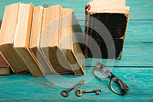 Old keys, glasses and stack of antique books on blue wooden desk
