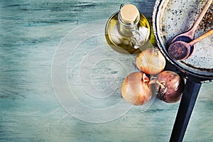 Old kitchen pan wooden spoon three onions carafe with olive oil on wooden table.