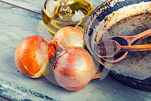 Old kitchen pan wooden spoon three onions carafe with olive oil on wooden table.