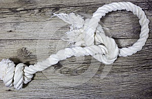 Old knoted rope lays on wooden background.
