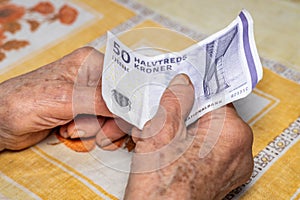 Old lady holds 50 Danish kroner in her hand, Denmark money, Cost of living in Denmark, Financial concept, Helping elderly people