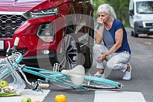 Old lady kneels beside her red car after she hits a biker