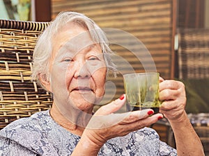 Old lady seated comfortably at home holding a cup of black coffee.