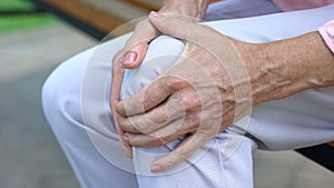 Old lady touching knee, sitting on bench, pain in joints, problems with knees