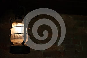 Old lamp hanging in dark room with brick wall behind