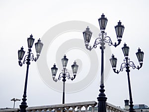 Old lampposts against the gray sky. Park lighting. Lanterns during the day