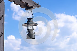 Old lantern hang on the wooden pole with cloudy blue sky in back