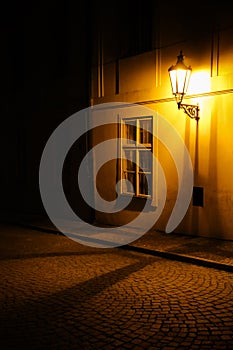 Old lantern illuminating a dark alleyway medieval street at night in Prague, Czech Republic. Low key photo