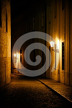 Old lanterns illuminating a dark alleyway medieval street at night in Prague, Czech Republic. Low key photo with brown yellow tone