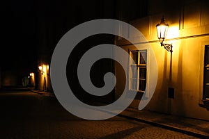 Old lanterns illuminating a dark alleyway medieval street at night in Prague, Czech Republic. Low key photo with brown yellow tone