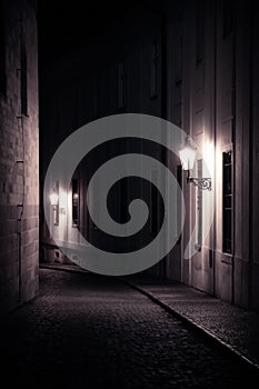 Old lanterns illuminating a dark alleyway medieval street at night in Prague, Czech Republic. Monochromatic photo in vertical.