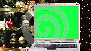 Old laptop with green screen and Christmas tree with blinking lights behind