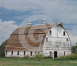 Old large white wooden barn with curved roof.