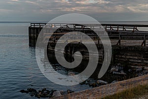 old large wooden pier stands on shore, coast of lake, seaside in the evening at sunset in water