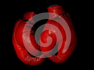 Old leather red boxing gloves hanging in the dark