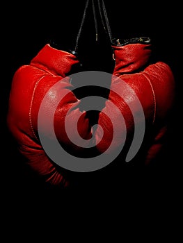 Old leather red boxing gloves hanging in the dark