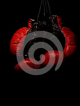 Old leather red boxing gloves hanging in the dark