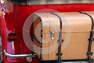 Old leather trunk attached to the red vintage car