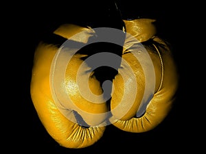 Old leather yellow boxing gloves hanging in the darkle