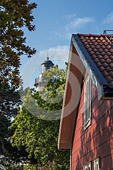 Old light house is covered with trees with red painted scandinavian style house in the front