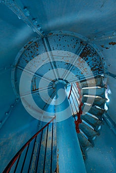 Old lighthouse on the inside. Red iron spiral stairs, round window and blue wall.