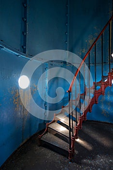 Old lighthouse on the inside. Red iron spiral stairs, round window and blue wall